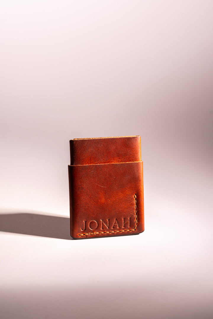 Brown leather wallet with 'JONAH' branding on a light pink background