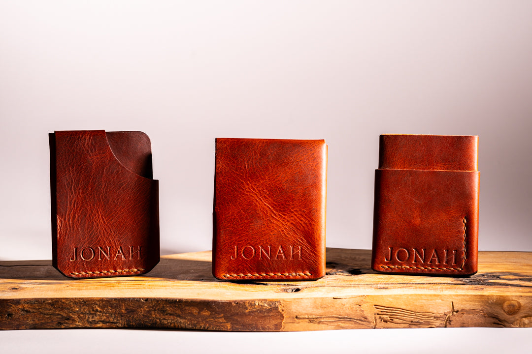 Three brown leather card holders with 'JONAH' embossed on them, placed on a wooden surface.